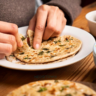 Hands tearing flatbread on plate